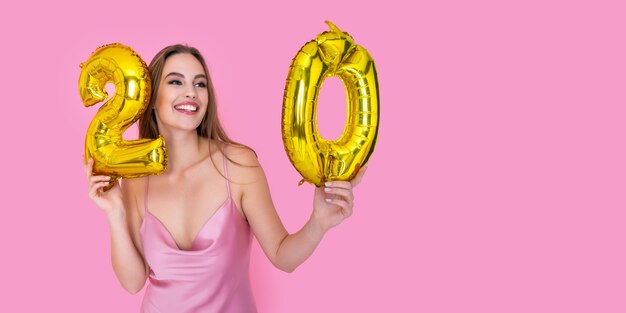 Młoda nastolatka szczęśliwa dziewczyna trzyma złoty balon foliowy na różowym tle koncepcji przyjęcia urodzinowego