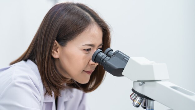 Młoda naukowiec kobieta w fartuchu laboratoryjnym patrząc przez mikroskop w laboratorium do prowadzenia badań i eksperymentów. Naukowiec pracujący w laboratorium. Edukacja pień fotografia