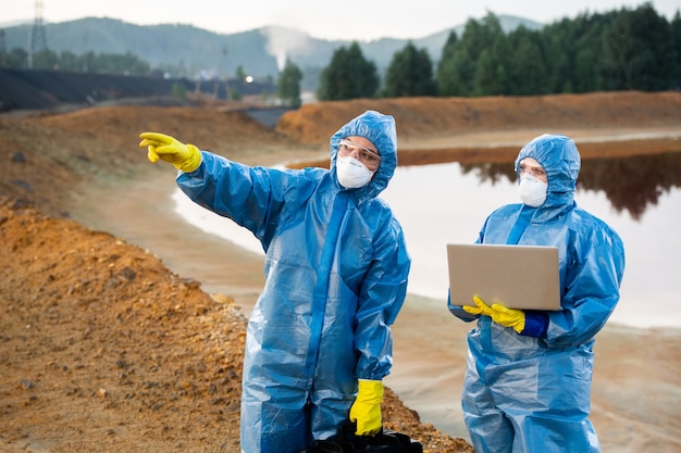 Młoda naukowiec wskazuje przed siebie, pokazując koledze z laptopem, gdzie należy pobrać próbki toksycznej gleby