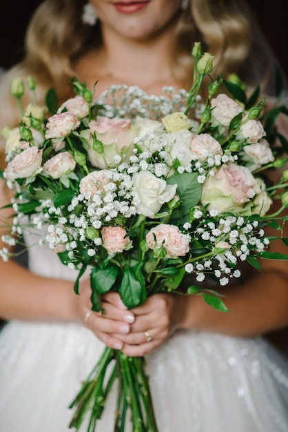 Młoda panna młoda w eleganckiej sukience stoi i trzyma bukiet różowych kwiatów i zieleni w przyrodzie