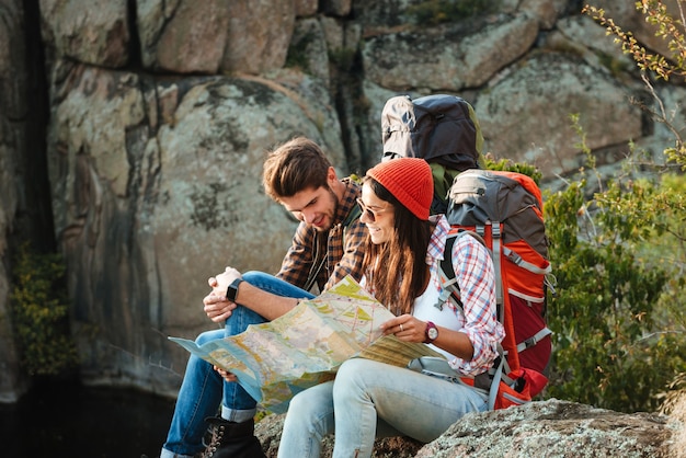 Młoda para Adventorous z mapą siedzi na zboczu spojrzeć na mapę