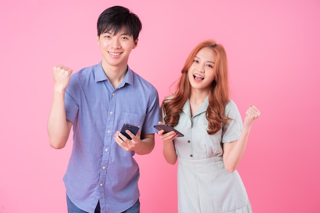Młoda para Azjatów korzystająca ze smartfona na różowym tle