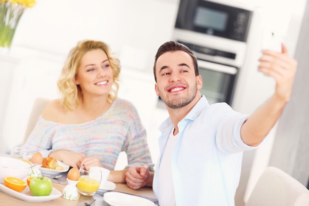 młoda para je śniadanie w kuchni i robi selfie