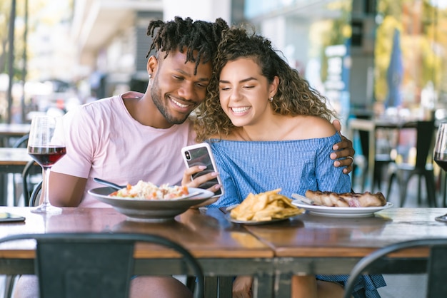 Młoda Para Korzystająca Z Telefonu Komórkowego I Spędzająca Wspólnie Czas Przy Obiedzie W Restauracji.