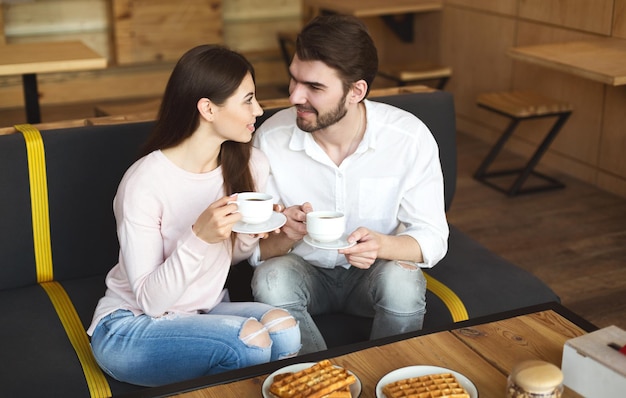 Młoda para millenialsów miłośnie patrzy na siebie w romantycznej atmosferze, kawiarnianym tle, kopiowej przestrzeni