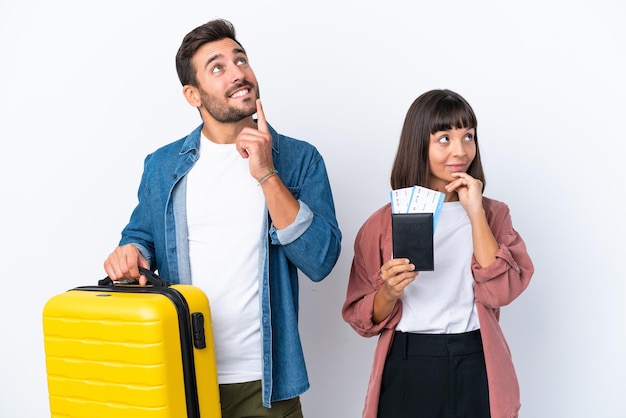 Młoda para podróżująca trzymająca walizkę i paszport na białym tle myśląca o pomyśle, patrząc w górę