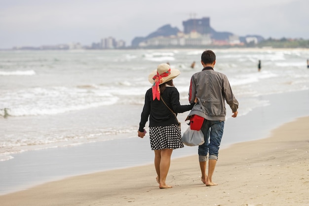 Młoda para przechodząca obok i trzymająca się za ręce na China Beach w Danang w Wietnamie. Bez twarzy