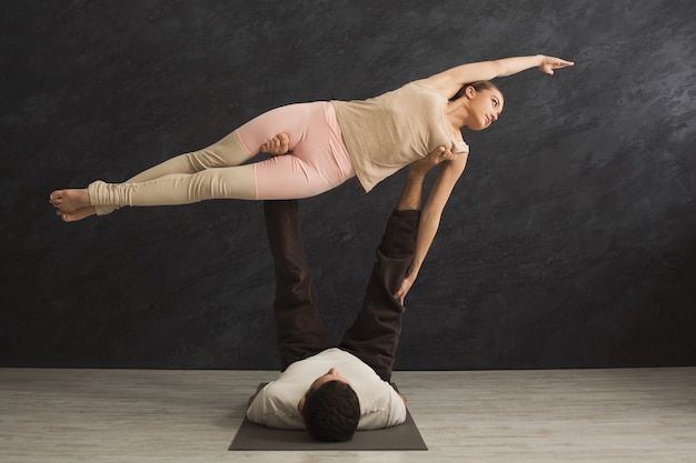 Młoda para razem uprawiania acroyoga na macie w siłowni. Kobieta latająca, kopia przestrzeń, widok z boku. Joga partnera, elastyczność, koncepcja zaufania