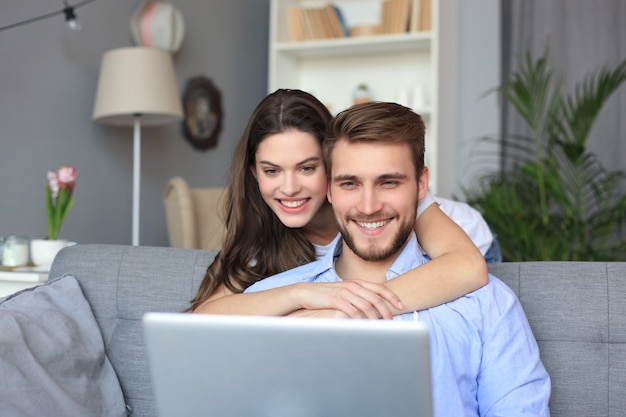 Młoda para robi zakupy online w domu, korzystając z laptopa na kanapie.