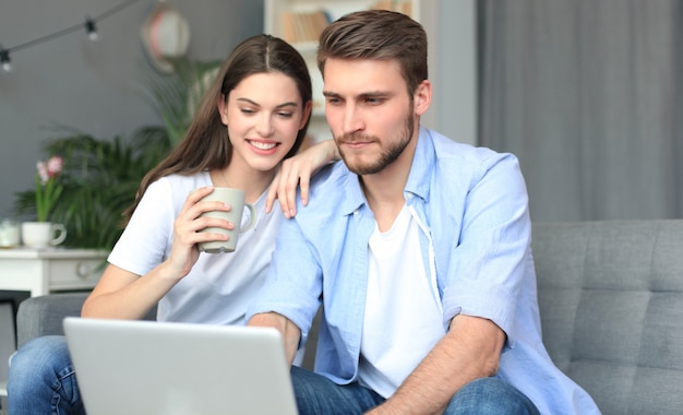 Młoda para robi zakupy online w domu, korzystając z laptopa na kanapie.