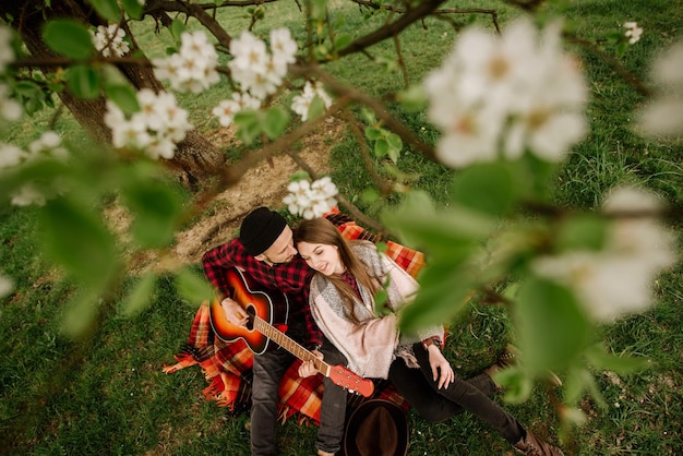 Młoda para siedząca pod wielkim drzewem i mężczyzna grający na gitarze