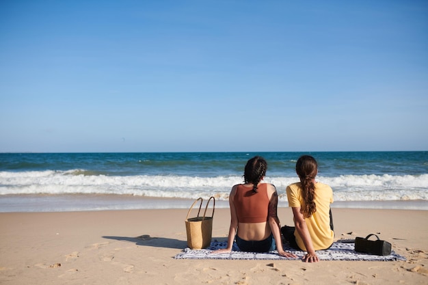 Młoda para siedzi na kocu na plaży i patrzy na falę morza od tyłu