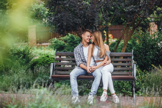 Zdjęcie młoda para siedzi na ławce w parku i patrząc na siebie. facet przytulający dziewczynę.