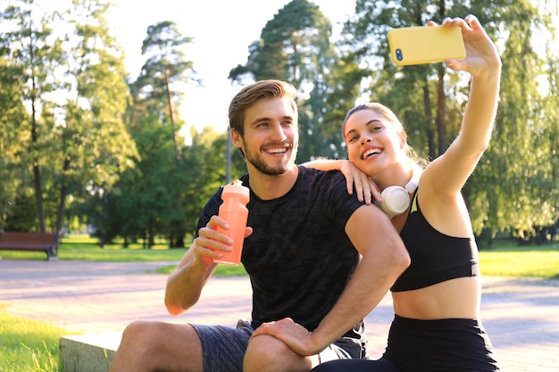 Młoda Para Sportowy W Sportowej Siedzi Na Parapecie W Parku Miejskim I Biorąc Selfie Po Treningu W Słoneczny Letni Dzień.