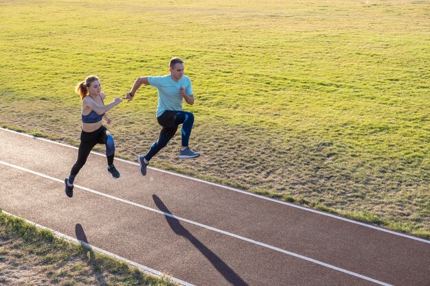 Młoda para sprawnych sportowców chłopiec i dziewczynka działa podczas ćwiczeń na czerwone ślady publicznego stadionu na zewnątrz.