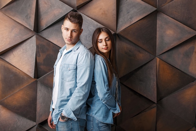 Młoda para stylowy w modne ubrania dżinsowe stoi w pobliżu drewnianej ściany