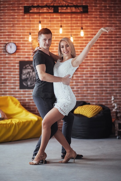 Młoda Para Tańczy Muzykę Latynoską: Bachata, Merengue, Salsa. Dwie Eleganckie Pozy W Kawiarni Z Ceglanymi ścianami