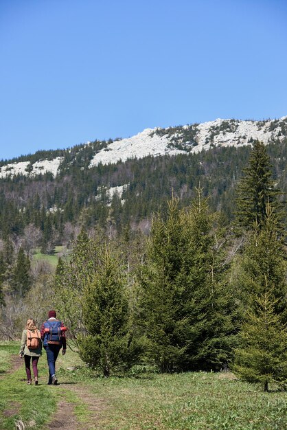 Młoda para trzymająca się za ręce i idąca ścieżką w kierunku dzikich lasów i białych skał w oddali