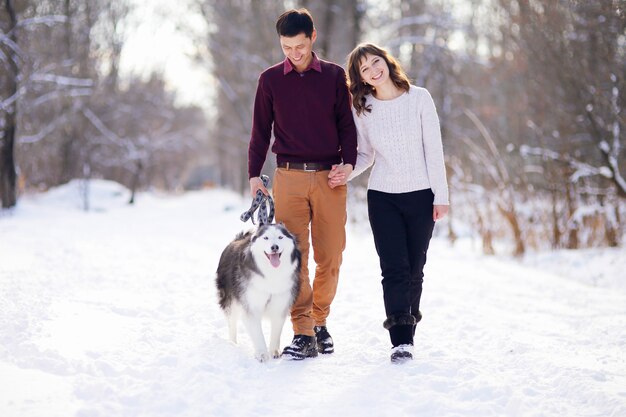 Młoda para uśmiecha się i bawi się w winter park z psem husky.