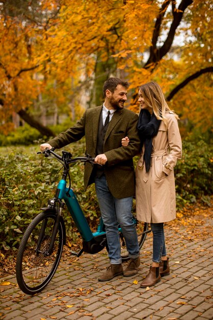 Młoda para w jesiennym parku z elektrycznym rowerem