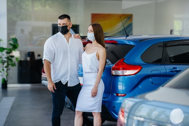 Młoda para w maskach wybiera nowy pojazd i konsultuje się z przedstawicielem salonu w okresie pandemii. Sprzedaż samochodów i życie w czasie pandemii.
