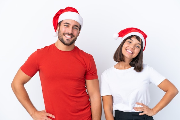 Młoda para w świątecznym kapeluszu na białym tle pozuje z rękami na biodrach i uśmiecha się