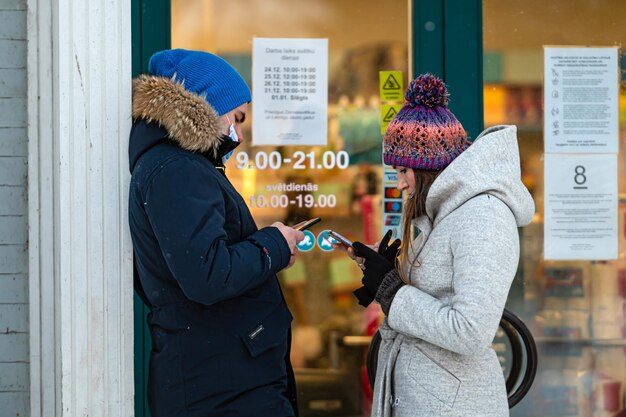 Młoda para w zimowych ubraniach stoi przy wejściu do sklepu i patrzy na smartfona