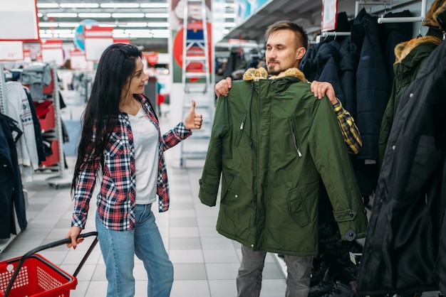 Młoda Para Wybiera Ciepłe Ubrania W Supermarkecie. Klienci Płci Męskiej I żeńskiej Na Rodzinne Zakupy. Mężczyzna I Kobieta Kupują Towary Do Domu