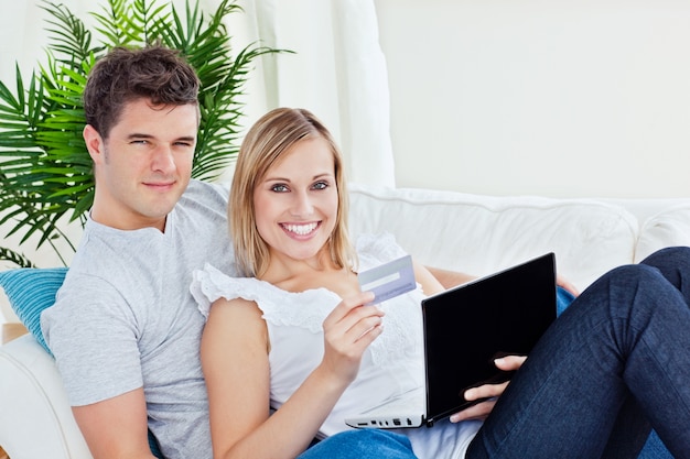 Młoda para z laptopa i karty kredytowej przez online leżącego w salonie