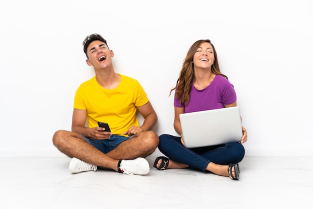 Młoda para z laptopa siedząc na podłodze na białym śmiechu