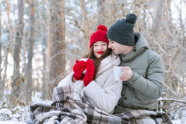 Młoda para zakochana w winter park owinięta w koc i pijąca herbatę. Sesja zdjęciowa z historią miłosną.