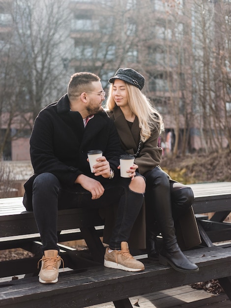 Młoda para zakochanych na świeżym powietrzu. Podróżni z filiżankami kawy spacerują po wiosennym parku. Piękny słoneczny dzień. Młoda para pije kawę na wynos