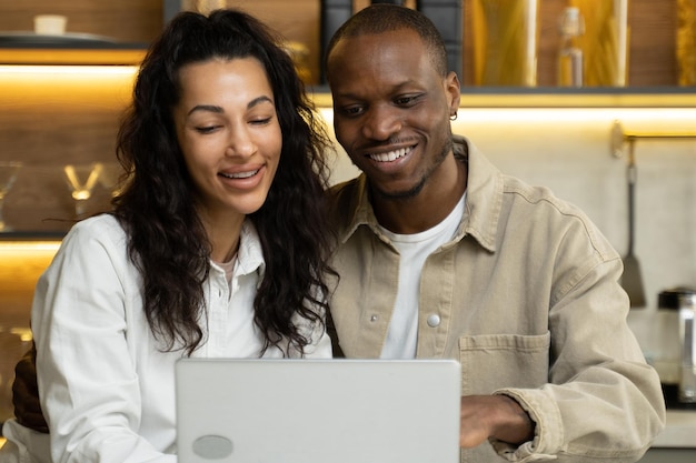 Młoda para zakochanych ogląda zdjęcia w laptopie przy kuchennym stole