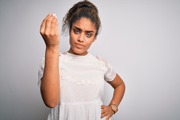 Młoda piękna Afroamerykanka ubrana w swobodną koszulkę stojąca nad białym tłem, wykonująca włoski gest ręką i palcami pewny siebie