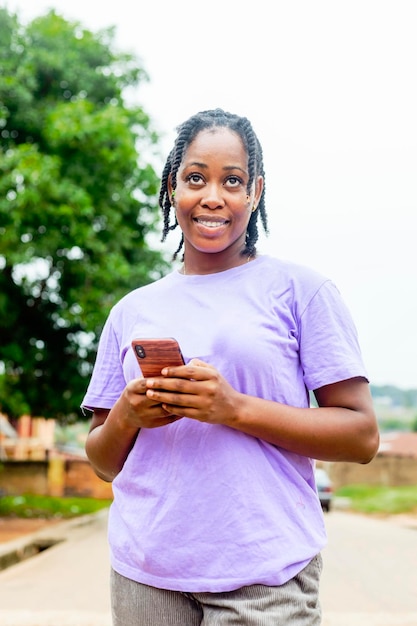Młoda piękna afrykańska dziewczyna trzyma telefon komórkowy i patrzy na kamerę
