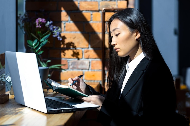 Młoda piękna Azjatka pracuje i studiuje w kawiarni, pracuje na laptopie, freelancerka pracuje zdalnie