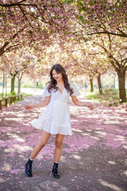 Młoda piękna Azjatka w białej sukni spaceruje po pełnym kwiatów parku. Sakura. Kwitnące drzewa. Wiosna.
