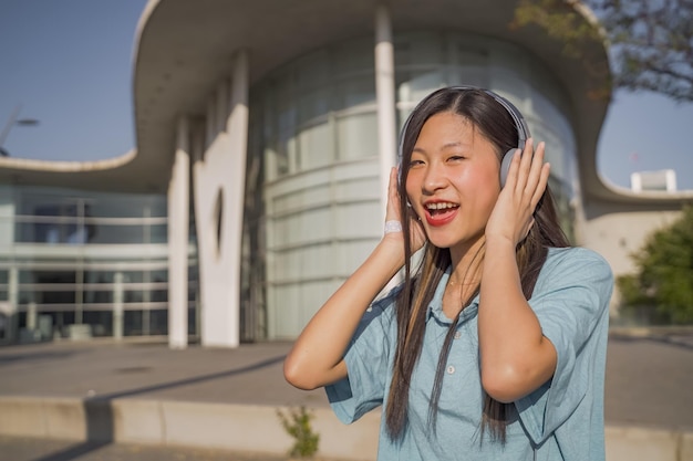 Młoda piękna azjatycka dziewczyna ze słuchawkami szczęśliwa uśmiechnięta i tańcząca na ulicy