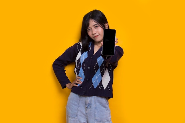 młoda piękna azjatycka kobieta demonstruje telefon komórkowy na białym tle na żółtym tle