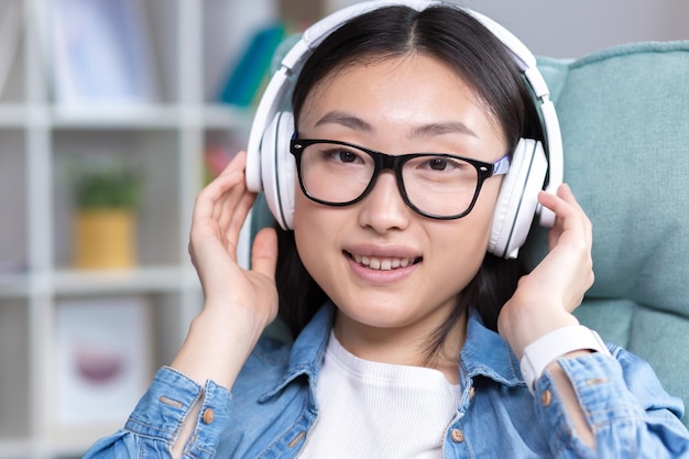 Młoda piękna azjatycka kobieta słucha muzyki w słuchawkach, zamykając oczy i rzucając rękami