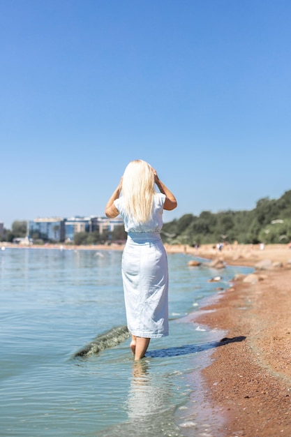 Młoda piękna blond włosa kobieta w niebieskiej sukience dżinsowej, patrząc na morze