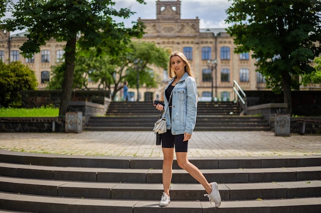 Młoda piękna blondynka w dżinsowej kurtce i obcisłych sportach