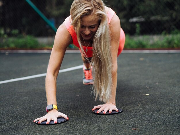 Zdjęcie młoda piękna blondynka z długimi włosami w neonowo-pomarańczowej odzieży aktywnej ćwiczy na podłodze