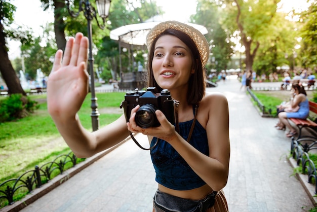 Zdjęcie młoda piękna brunetka dziewczyna w kapeluszu uśmiecha się, robienia zdjęć w parku.