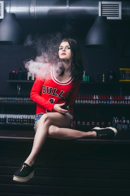 Młoda piękna brunetka kobieta z modnym makijażem w barze z parą z elektronicznego papierosa
