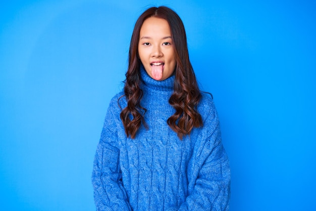 Młoda piękna Chinka ubrana w swobodny zimowy sweter wystający język zadowolona z zabawnego wyrazu twarzy. koncepcja emocji.