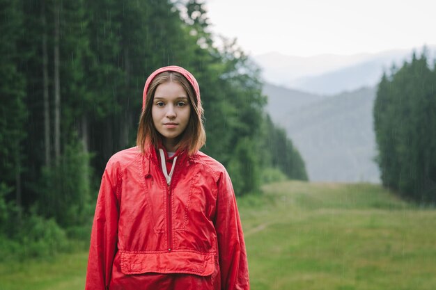 młoda piękna dama stojąca na górskim wzgórzu w strugach deszczu, ubrana w czerwoną wodoodporność