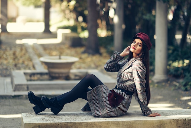 Młoda piękna dziewczyna jest ubranym żakieta i nakrętki zimy obsiadanie na ławce w miastowym parku.