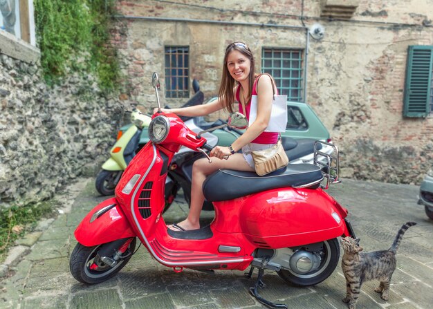 Młoda piękna dziewczyna jeździ czerwonym motocyklem Vespa ulicami Rzymu we Włoszech.