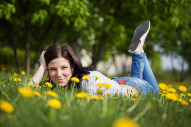 Młoda piękna dziewczyna leży na trawie. Lato pole z kwiatów dandelion